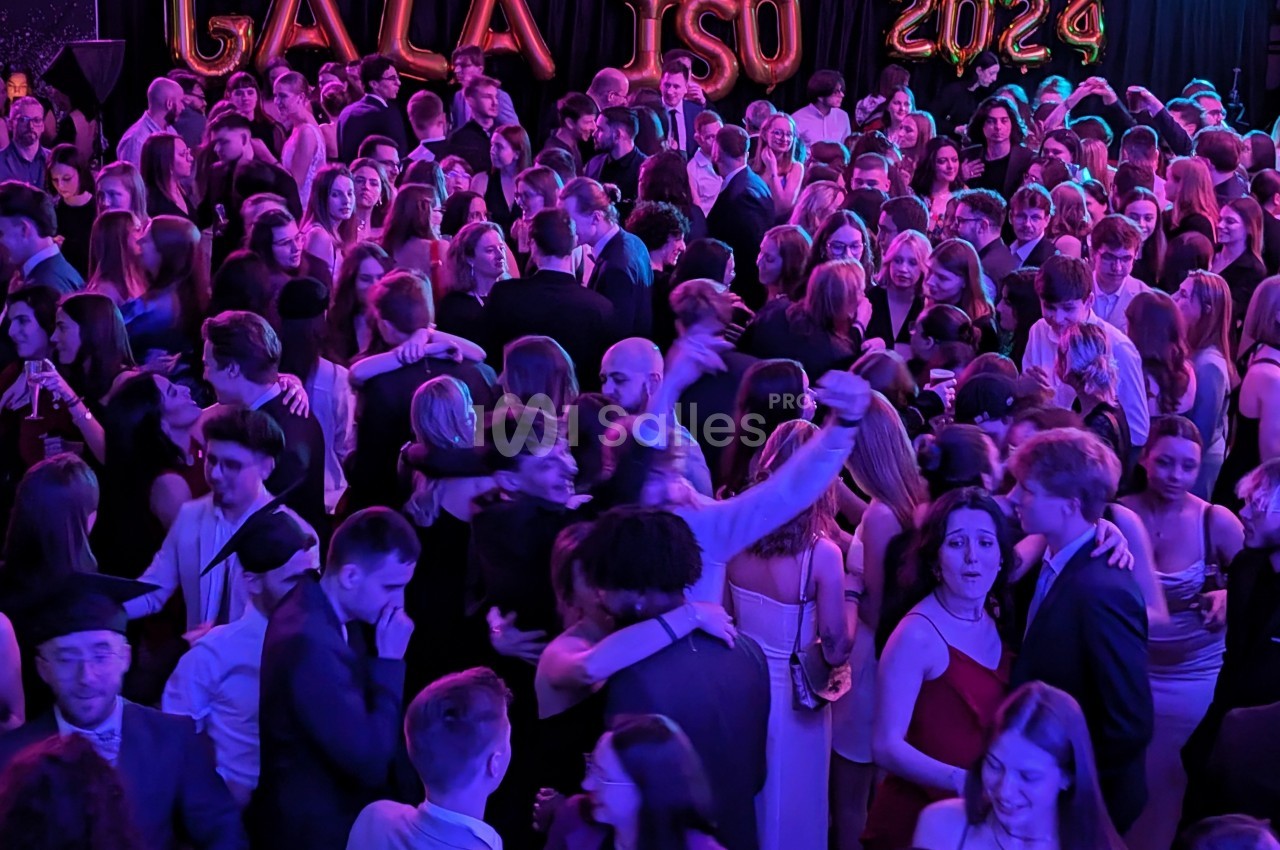 Des personnes dansant et discutant lors d'une soirée festive avec des ballons formant ’GALA ISO 2024’ en arrière-plan.