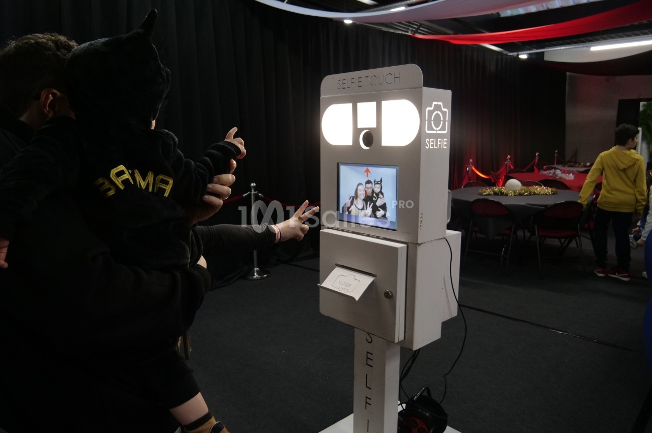 Une borne photo interactive utilisée par des personnes dans un espace intérieur décoré avec des tables et des rideaux.