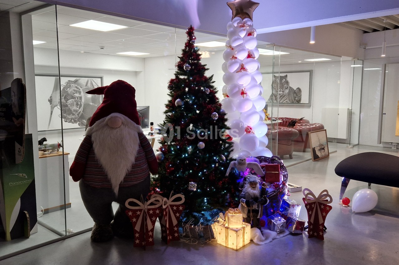 Décoration de Noël avec un sapin illuminé, un gnome, des cadeaux et un arbre en ballons dans un espace moderne.