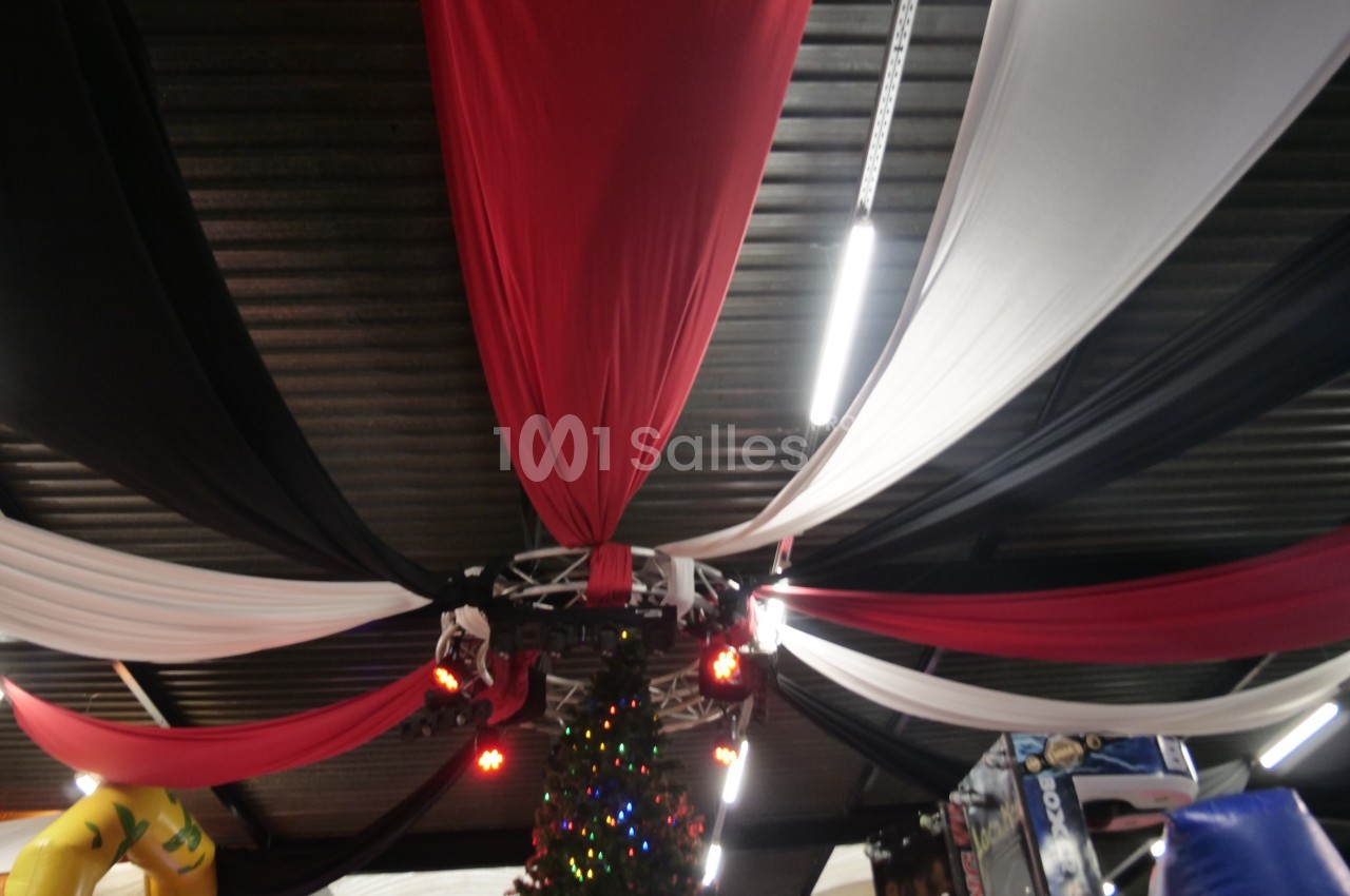 Tissu rouge, noir et blanc suspendu au plafond d'un espace intérieur, avec un sapin décoré en dessous.