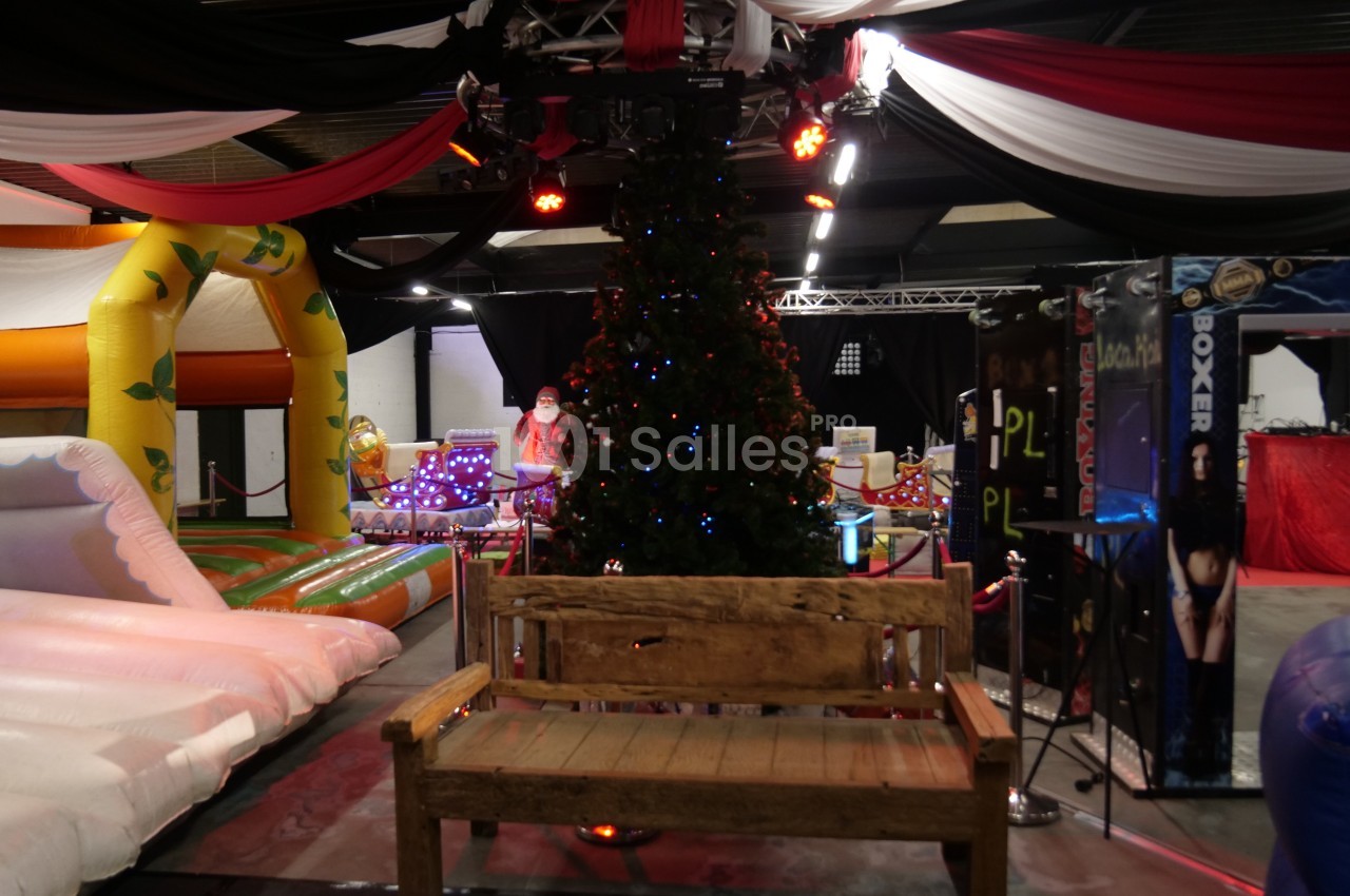Banc en bois devant un sapin de Noël décoré, entouré de structures gonflables et d'éléments festifs en intérieur.