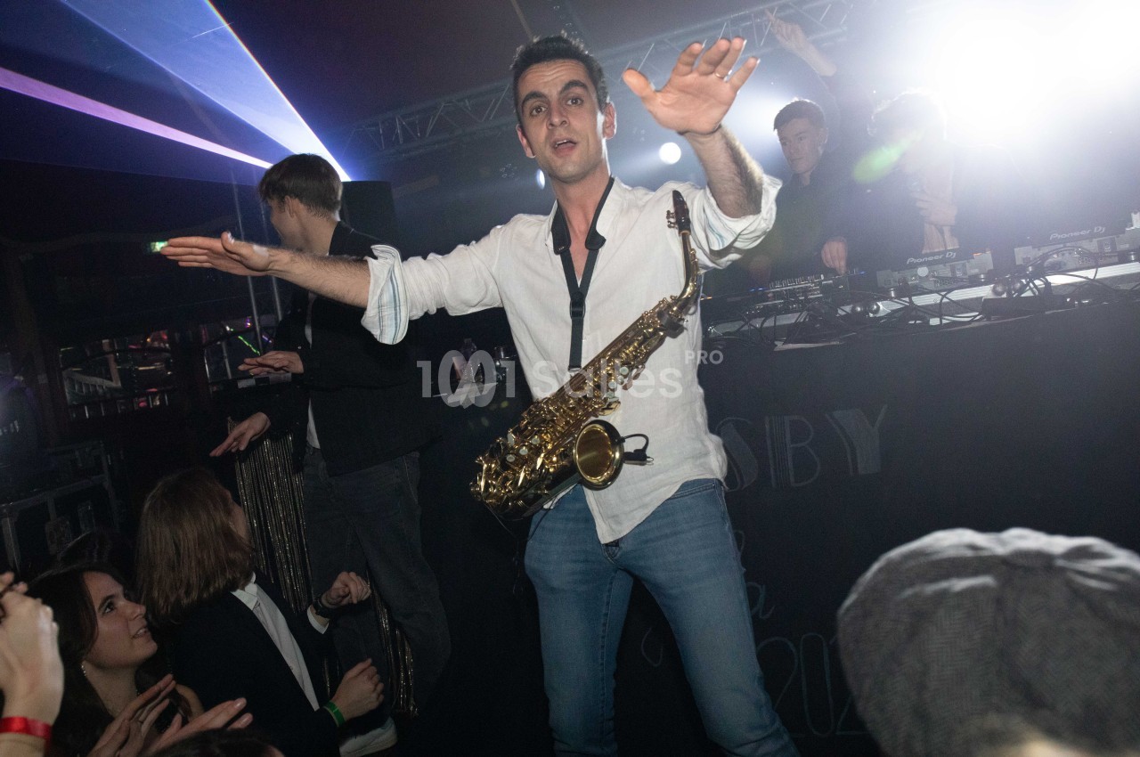 Un musicien jouant du saxophone sur scène, entouré d'un public et d'une ambiance lumineuse festive.