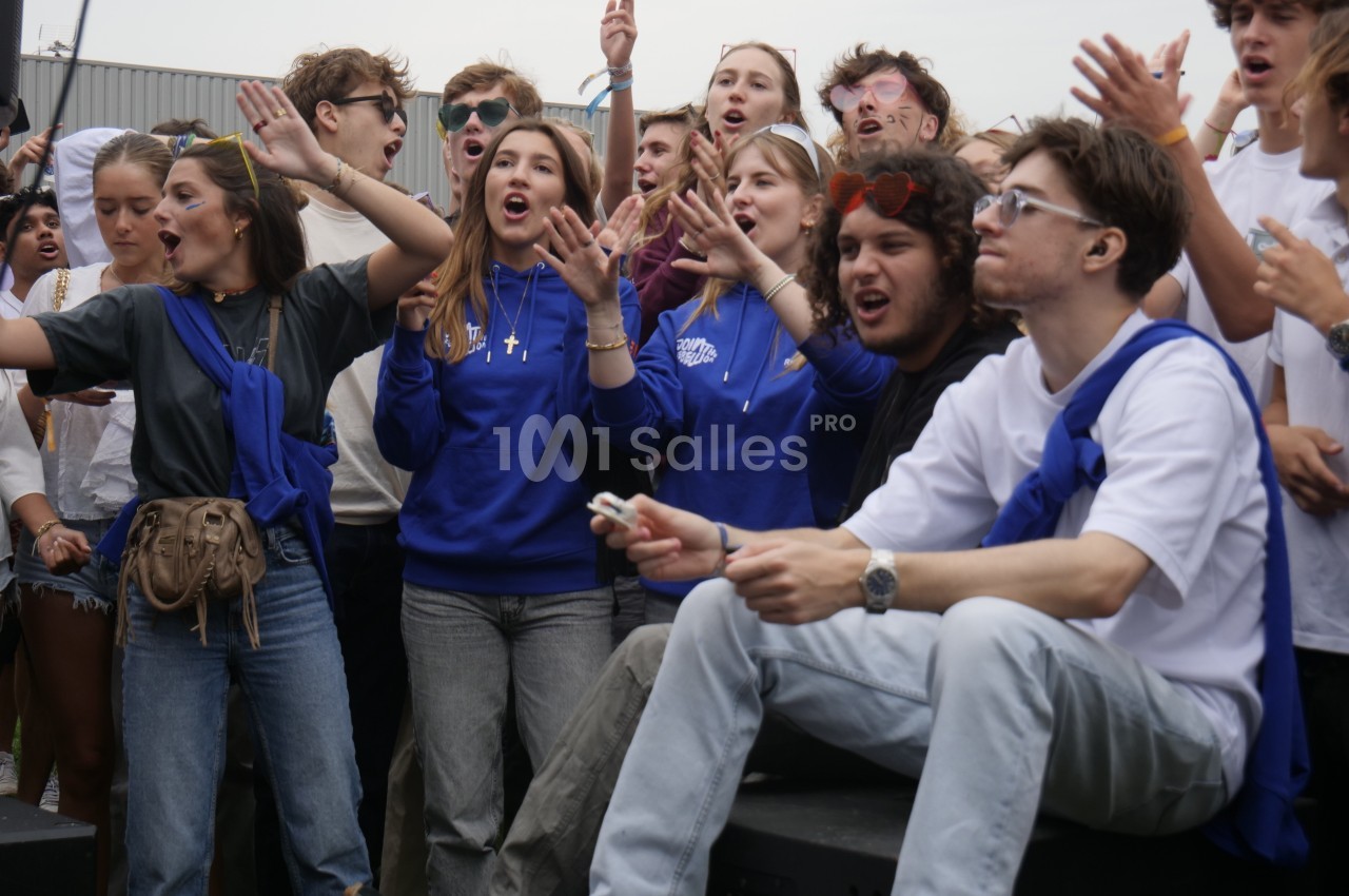 Un groupe de jeunes exprime de l'enthousiasme et chante ensemble en extérieur lors d'un événement.