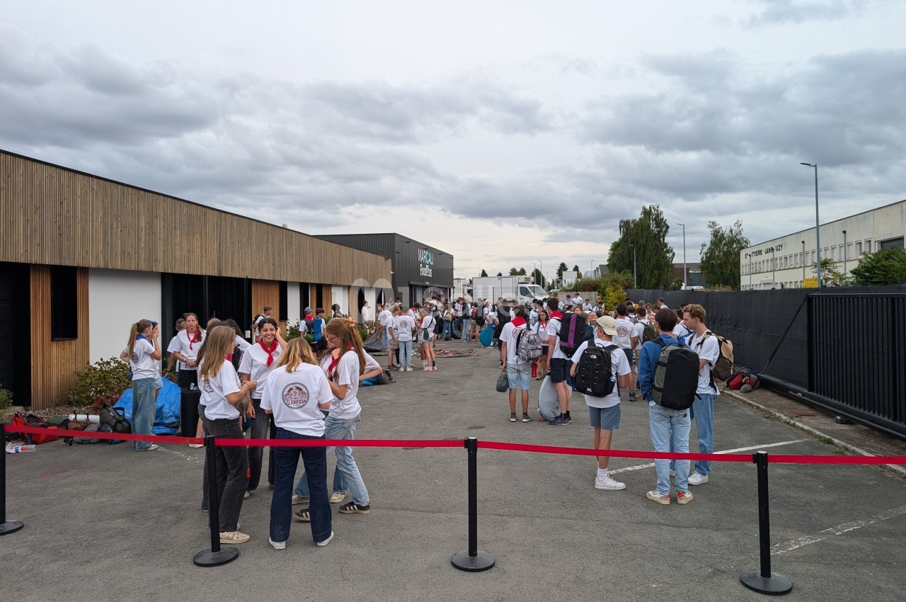 Des personnes rassemblées à l'extérieur d'un bâtiment moderne, discutant par petits groupes sous un ciel nuageux.