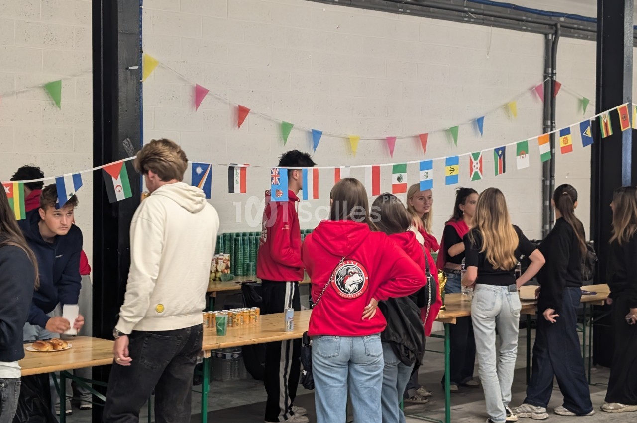 Des personnes discutent et se servent à des stands décorés de guirlandes de drapeaux dans un espace intérieur.