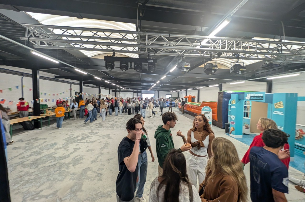 Des personnes discutent et se déplacent dans un grand espace intérieur éclairé, aménagé avec des stands et des décorations.