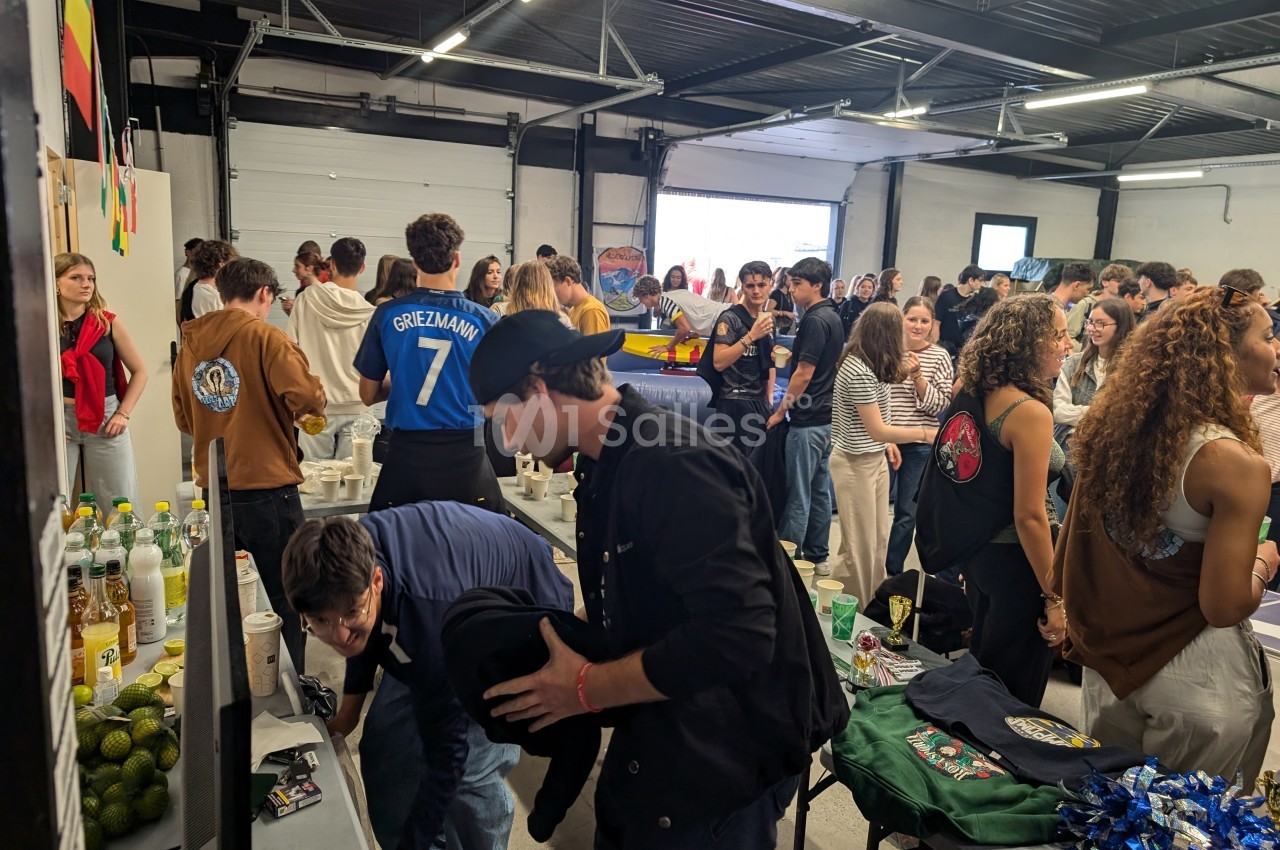 Des personnes rassemblées dans une salle, certaines discutent ou regardent des stands avec des produits et des boissons.