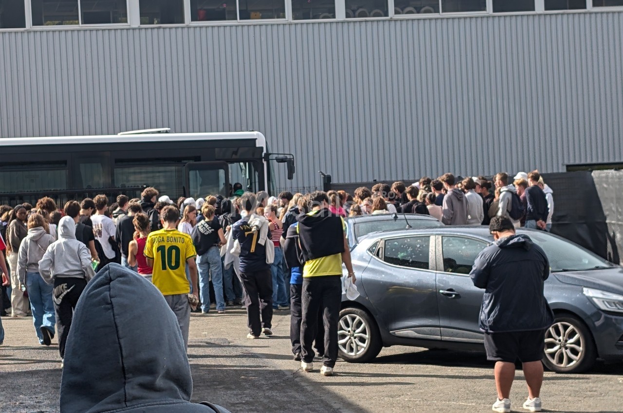 Un groupe de personnes rassemblées près d'un bus stationné devant un bâtiment industriel.