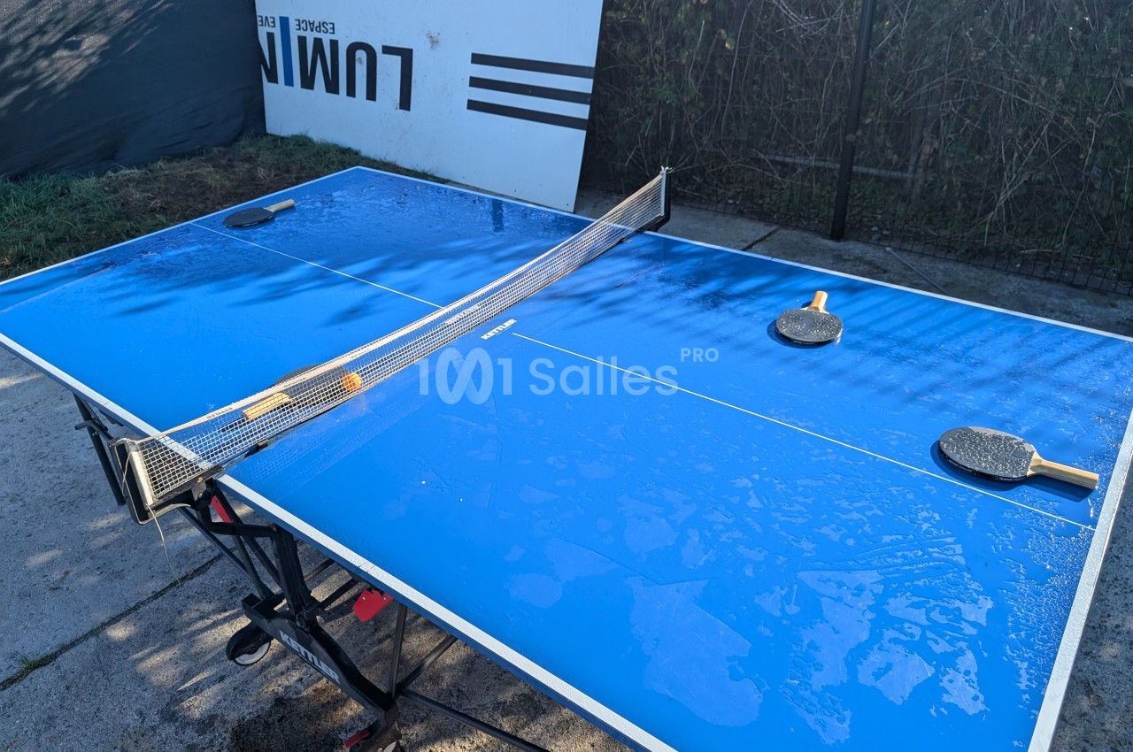 Table de ping-pong bleue en extérieur avec deux raquettes posées, surface mouillée par la rosée.