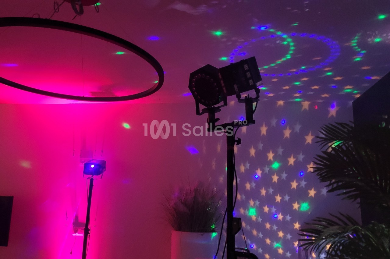 Projecteurs colorés illuminant une pièce sombre avec des motifs étoilés et des plantes en arrière-plan.