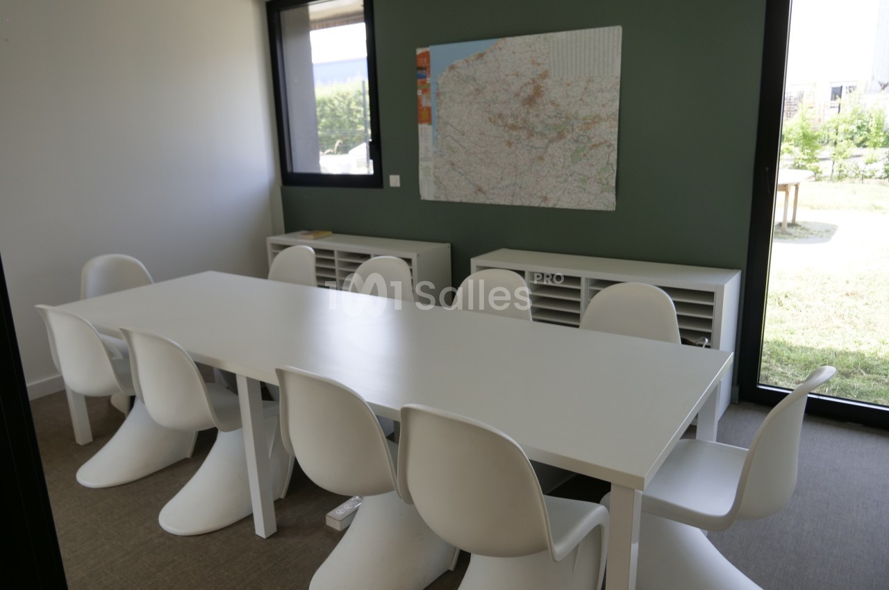 Salle de réunion lumineuse avec une grande table blanche, des chaises design et une carte accrochée au mur vert.