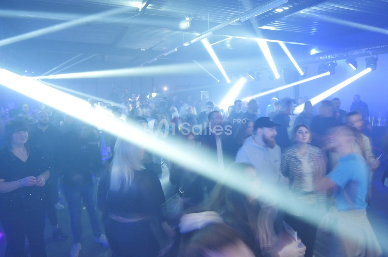 Des personnes dans une salle sombre participent à un événement avec des éclairages lumineux et des faisceaux de lumière.