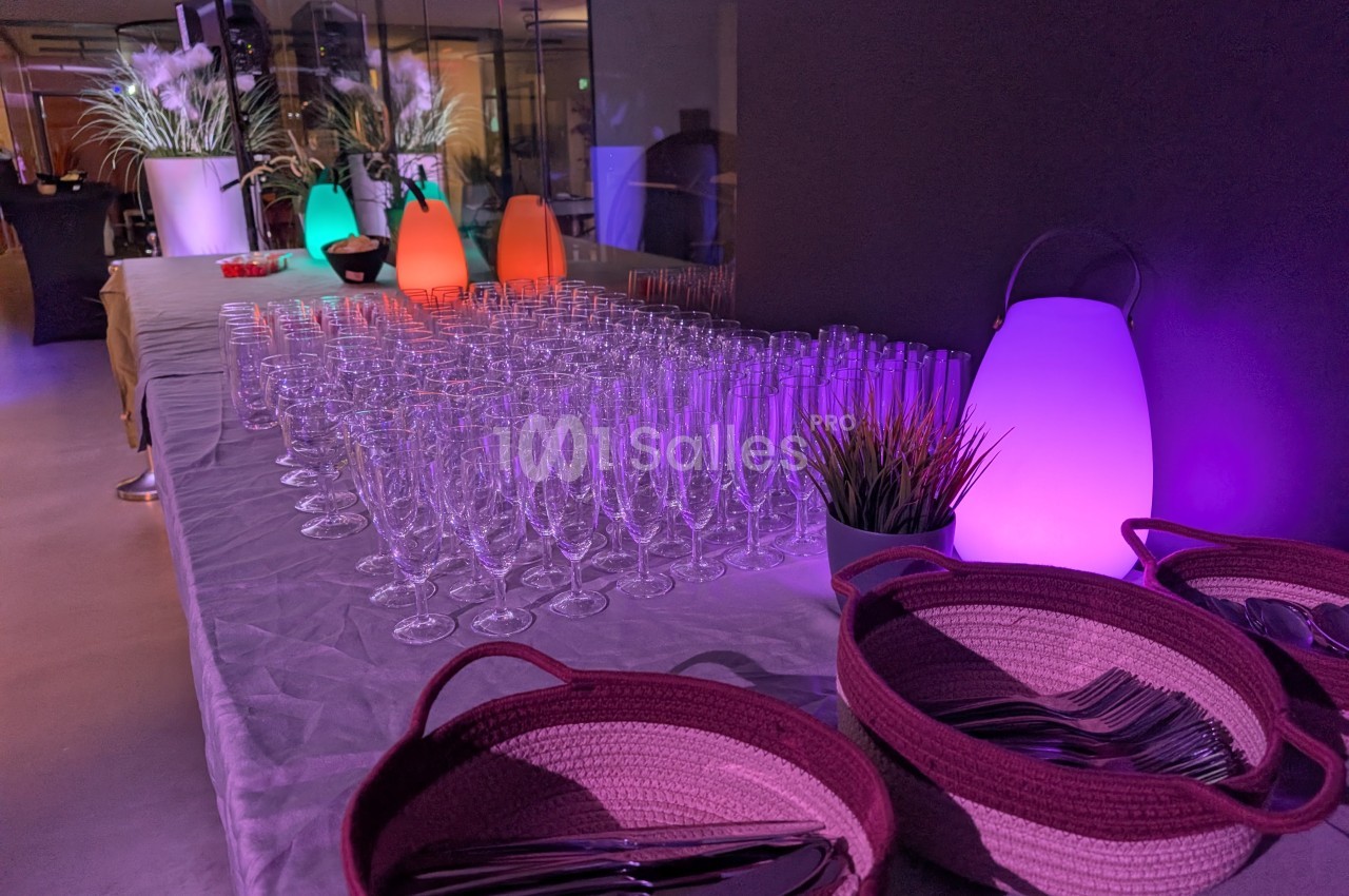 Table dressée avec des verres à pied, paniers contenant des couverts et éclairage coloré dans une ambiance tamisée.
