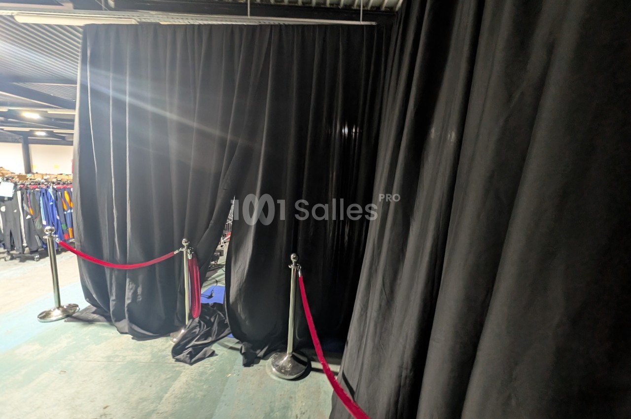 Rideaux noirs ouverts dans un espace industriel, délimitant une zone avec des cordons rouges et poteaux chromés.