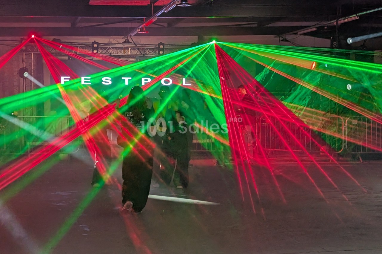 Des faisceaux laser rouges et verts illuminent une salle sombre avec des personnes en arrière-plan.