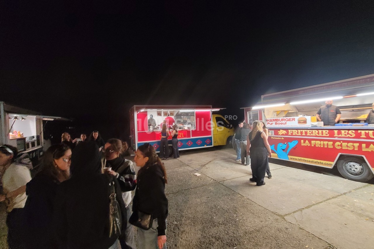 Des food trucks éclairés servent des clients rassemblés en soirée sur un espace extérieur sombre.