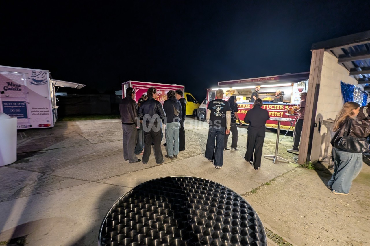 Des personnes font la queue devant des stands de nourriture éclairés la nuit dans un espace extérieur.