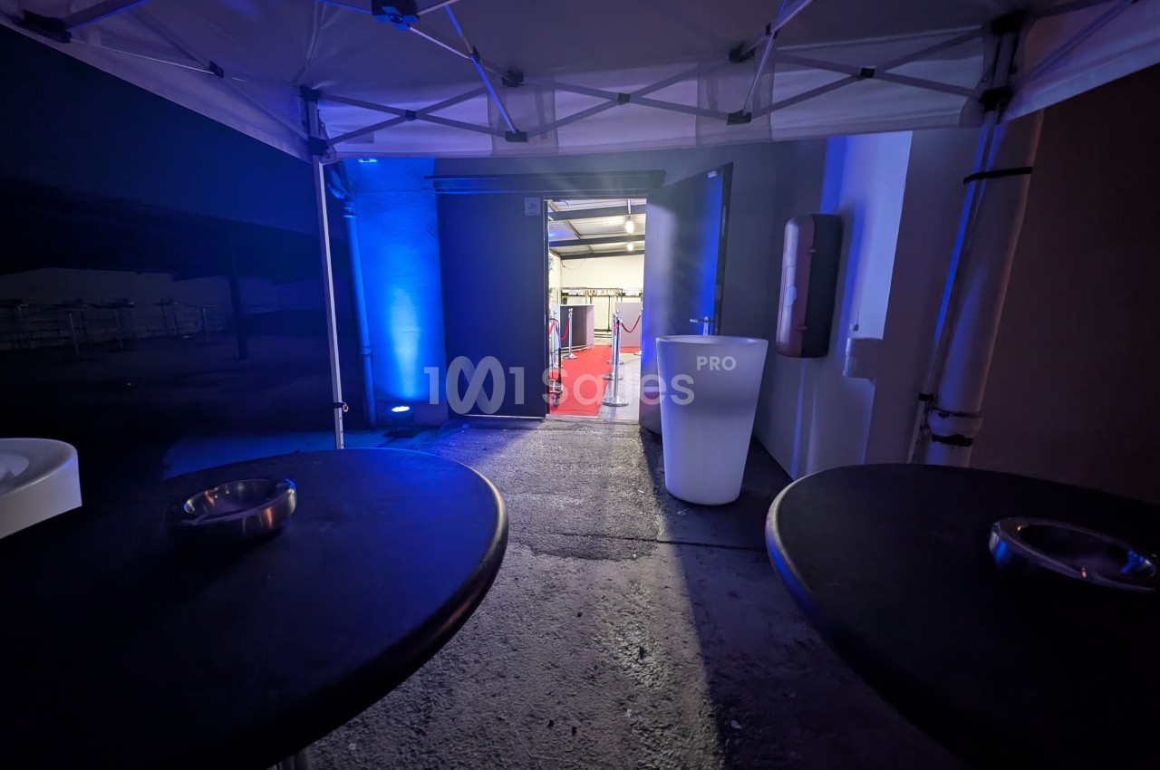 Vue depuis l'intérieur d'une tente éclairée en bleu, donnant sur un couloir avec un tapis rouge.