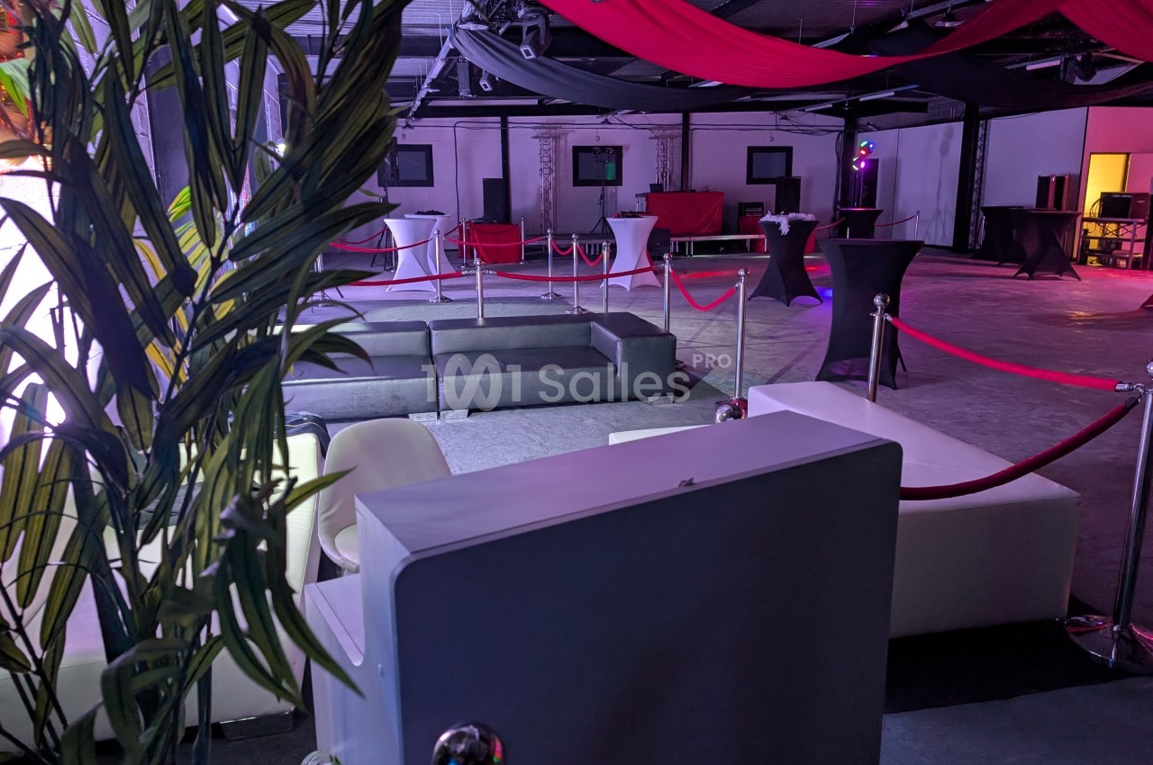 Espace événementiel intérieur avec canapés, tables hautes, cordons rouges et éclairage tamisé.