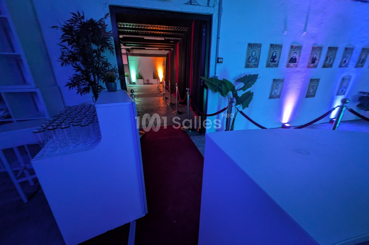 Entrée d'une salle éclairée par des lumières colorées, avec tapis rouge, cordons de sécurité et décorations murales.