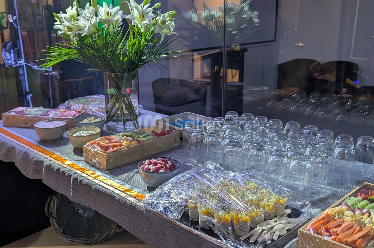 Table de buffet avec verrines, légumes, charcuterie, pains, fleurs blanches en vase et rangée de verres vides.