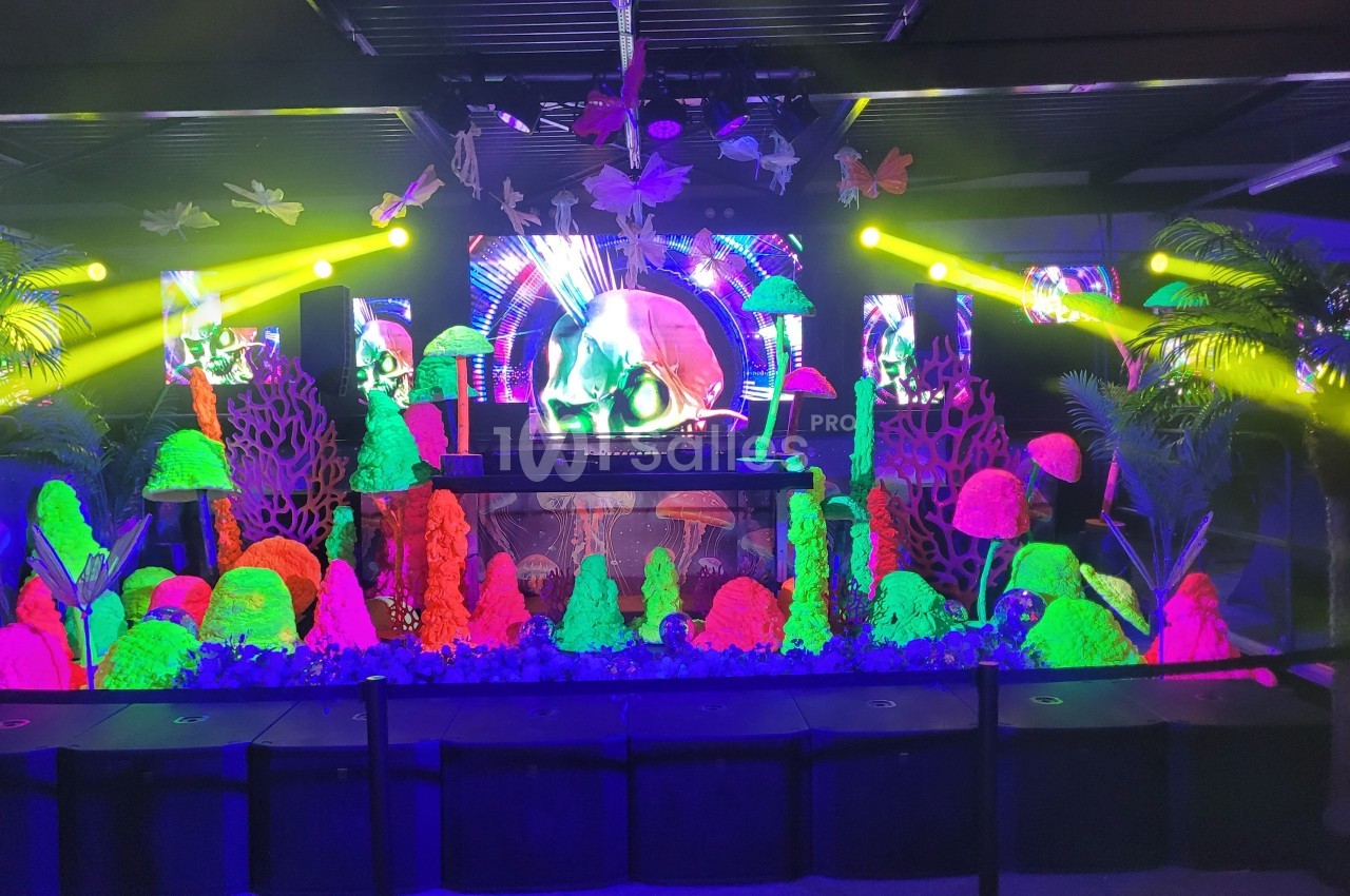 Scène décorée de champignons fluorescents, plantes tropicales et éclairages colorés dans une ambiance festive.