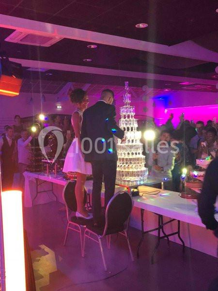 Un couple debout sur des chaises remplit une pyramide de coupes en verre lors d'une réception festive.
