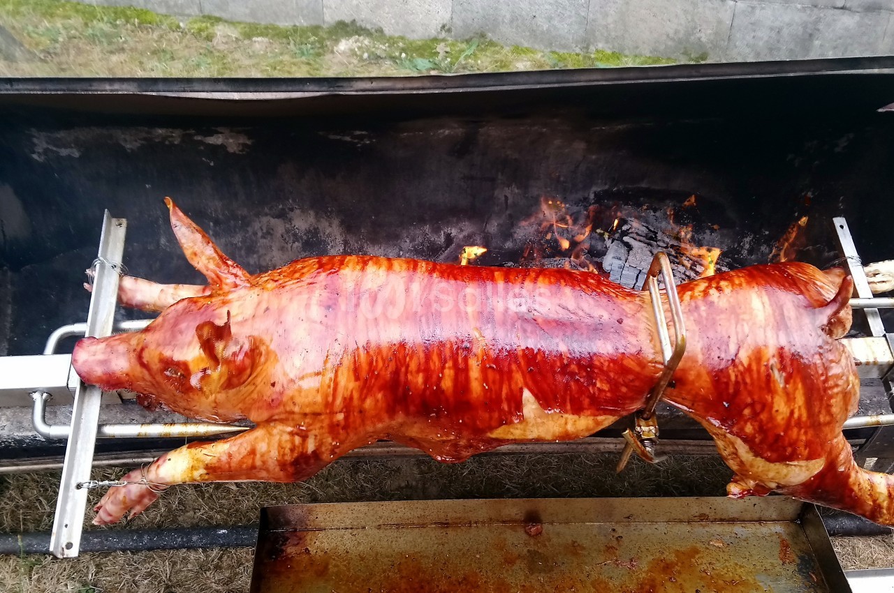 Porc entier rôti à la broche au-dessus d'un feu de bois, avec une peau dorée et croustillante.