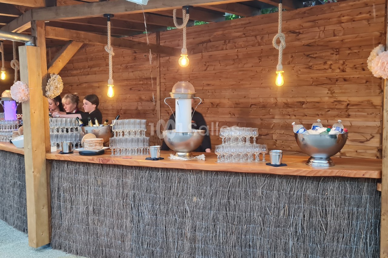 Un stand en bois avec des verres empilés, une fontaine à boissons et des bols contenant des glaçons et des bouteilles.