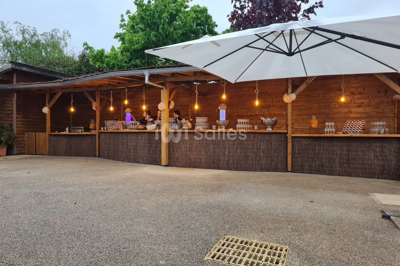 Comptoir en bois extérieur avec boissons et décorations lumineuses, abrité par un grand parasol blanc.