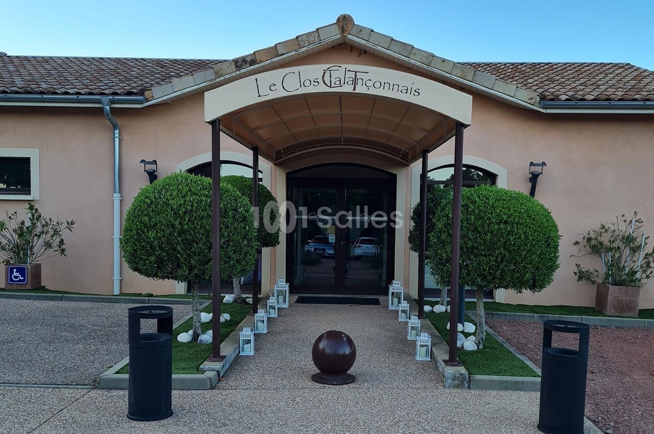 Entrée d'un bâtiment avec une arche portant l'inscription ’Le Clos Talançonnais’, entourée de buissons taillés et lanternes.