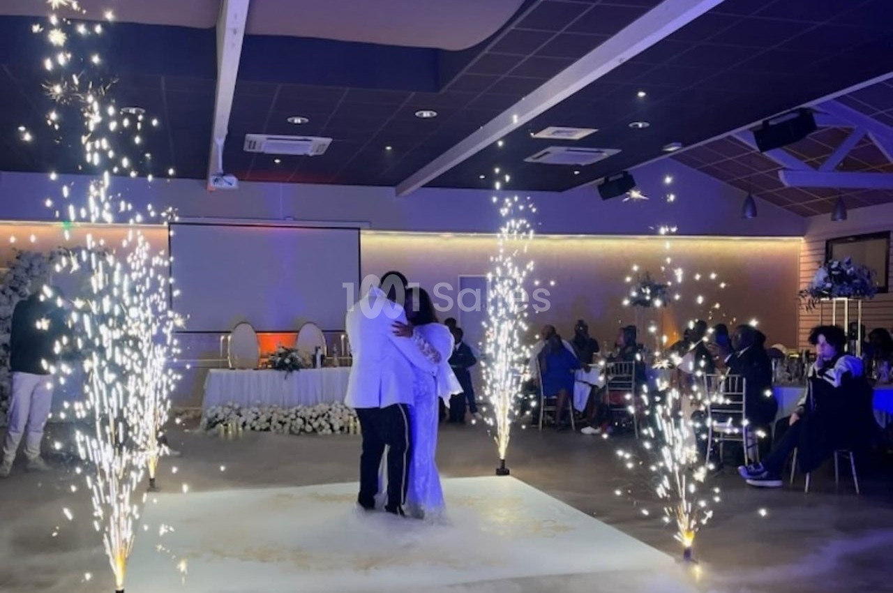 Un couple danse au centre d'une salle de réception illuminée par des fontaines d'étincelles, entouré d'invités assis.