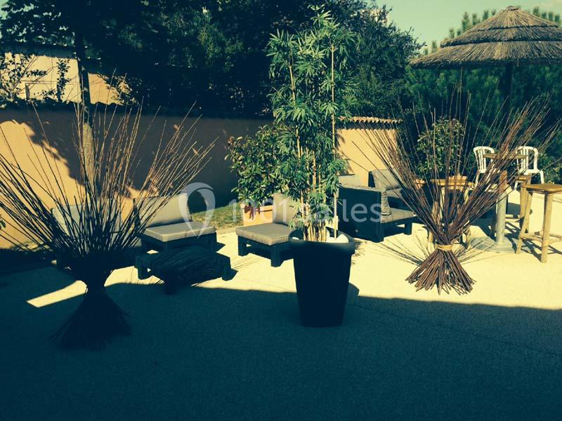 Mobilier de jardin avec fauteuils, tables et décorations végétales sur une terrasse ensoleillée.