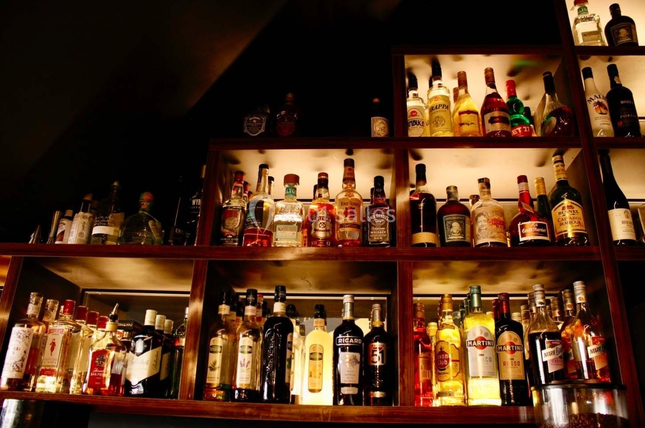 Étagères en bois remplies de bouteilles d'alcool variées, éclairées par une lumière chaude.
