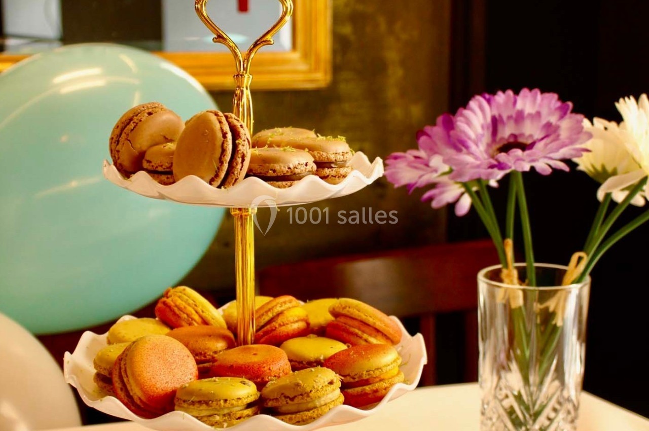 Plateau à deux étages rempli de macarons colorés, posé sur une table décorée de fleurs et de ballons.