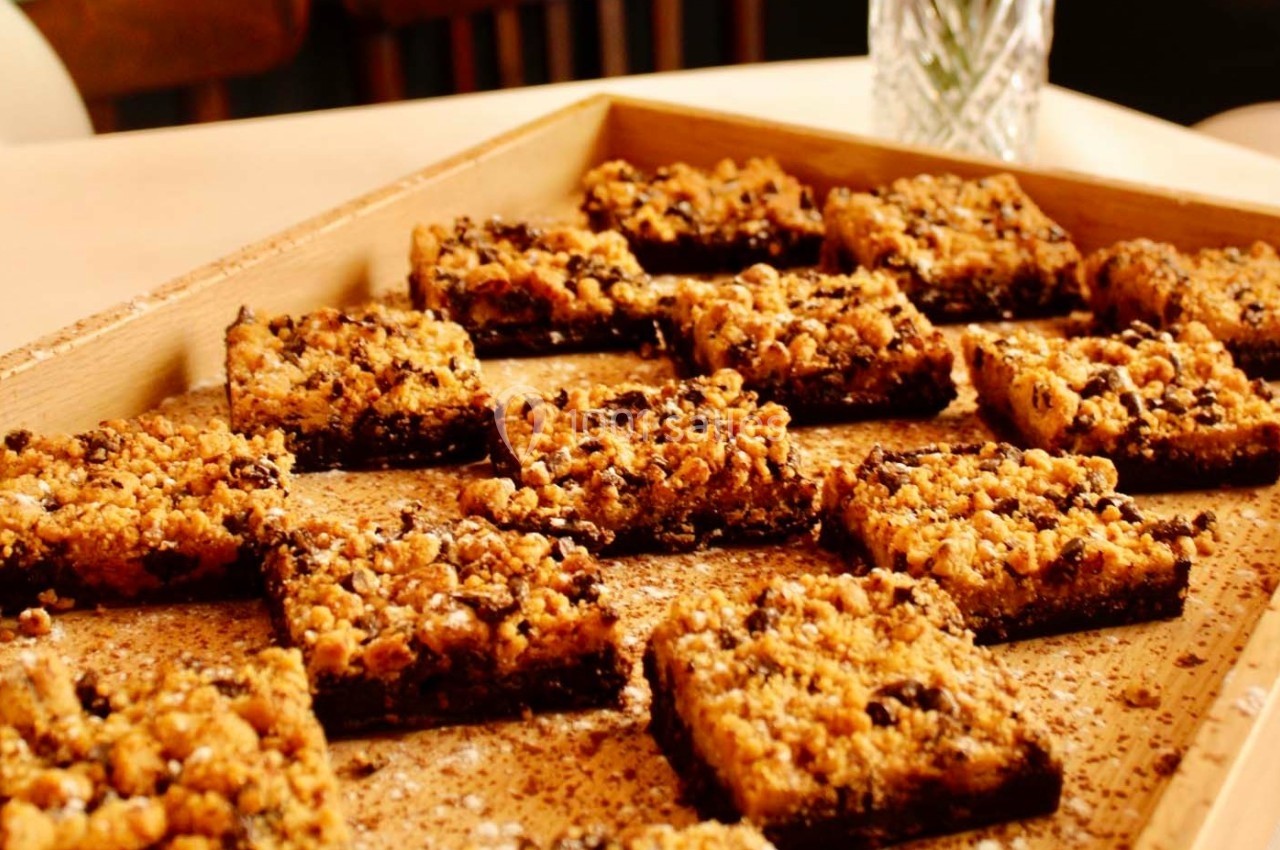 Carrés de crumble dorés disposés sur un plateau en bois, saupoudrés de sucre ou d'épices.