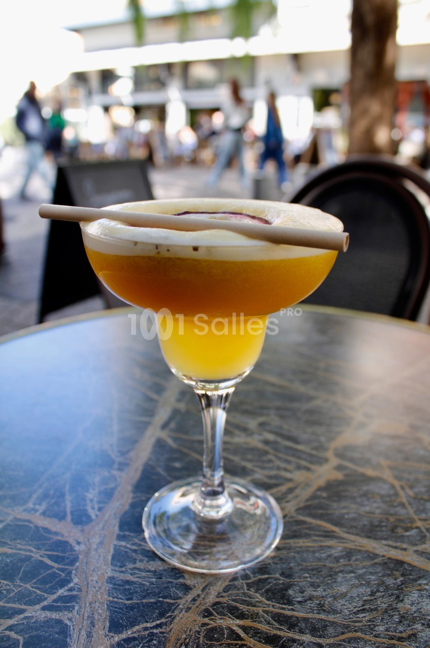Verre de cocktail jaune sur une table en marbre, garni de mousse et d'une décoration en bois, en extérieur.