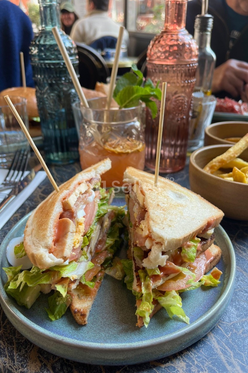 Sandwich club garni de salade, tomate et poulet, servi avec des frites et une boisson sur une table de restaurant.