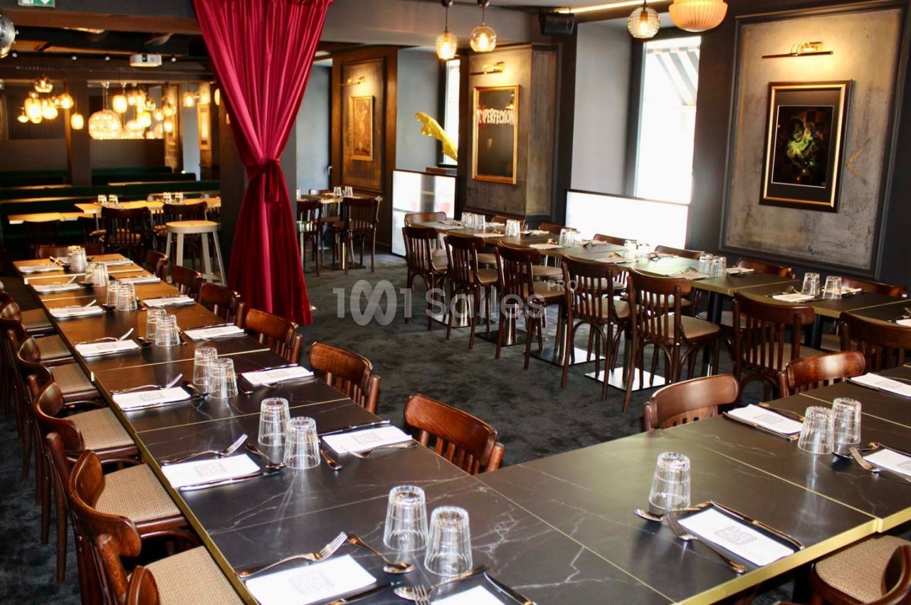 Salle de restaurant élégante avec de longues tables dressées, des chaises en bois et une décoration lumineuse.