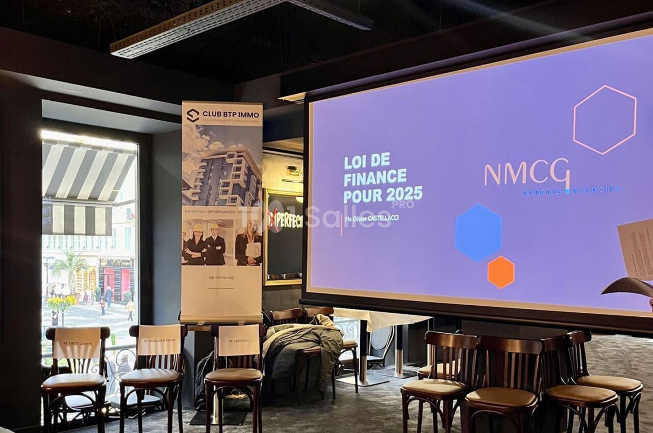 Salle de conférence avec un écran affichant ’Loi de finance pour 2025’, des chaises alignées et une bannière promotionnelle.