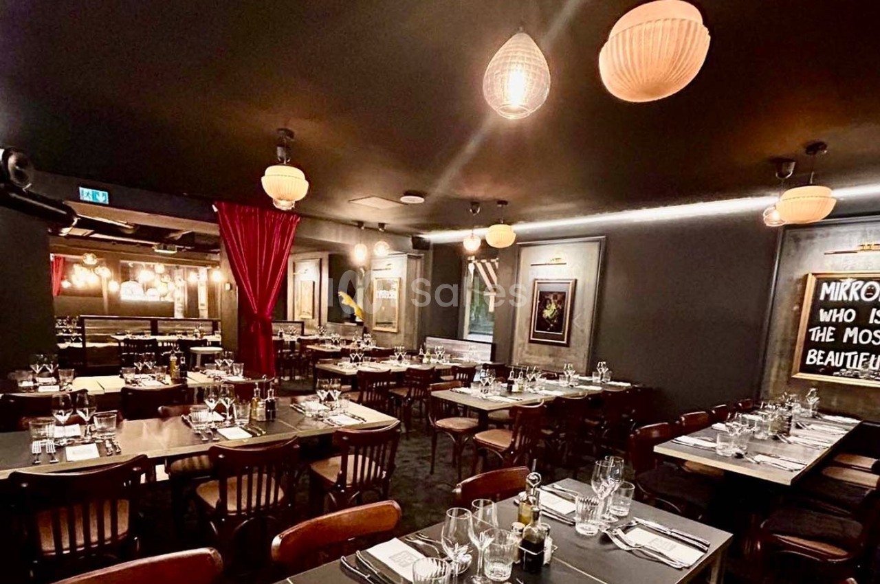 Salle de restaurant élégante avec tables dressées, éclairage tamisé et rideaux rouges en arrière-plan.