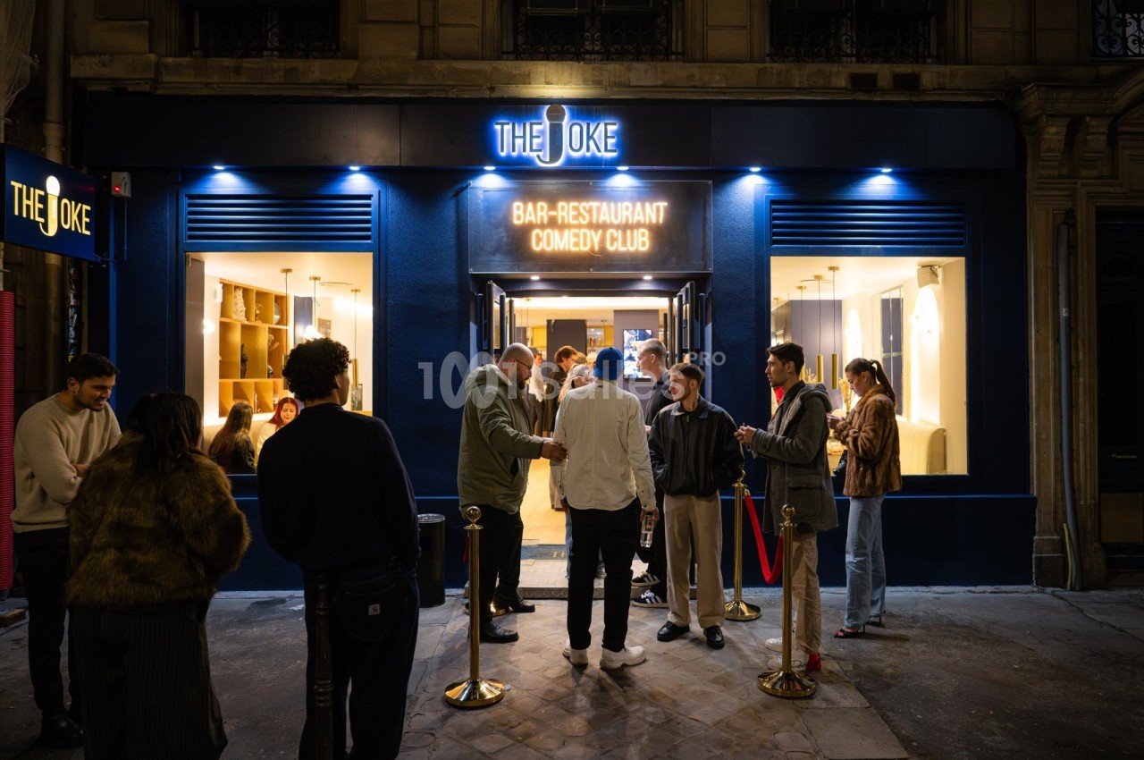Façade d'un bar-restaurant avec enseigne lumineuse, des clients discutent devant l'entrée en soirée.