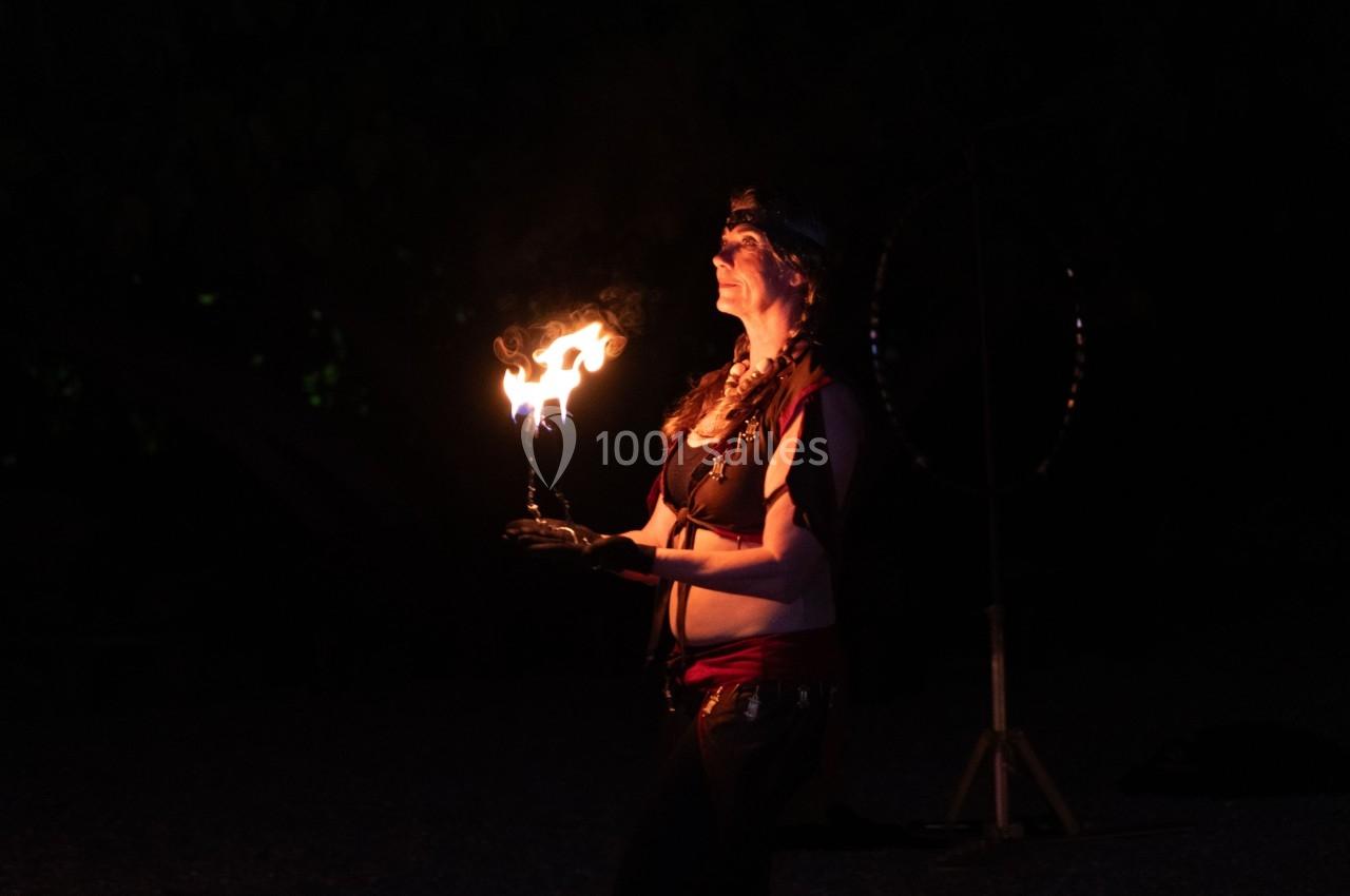 Une femme jongle avec une flamme dans l'obscurité, vêtue de tenues de spectacle.