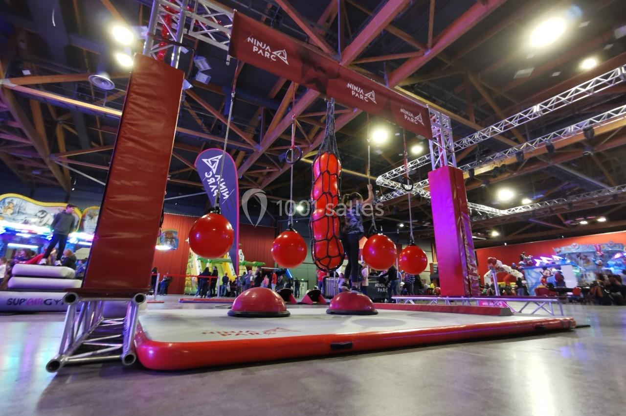 Parcours d'obstacles intérieur avec structures suspendues, ballons rouges et plateformes dans un espace de loisirs.