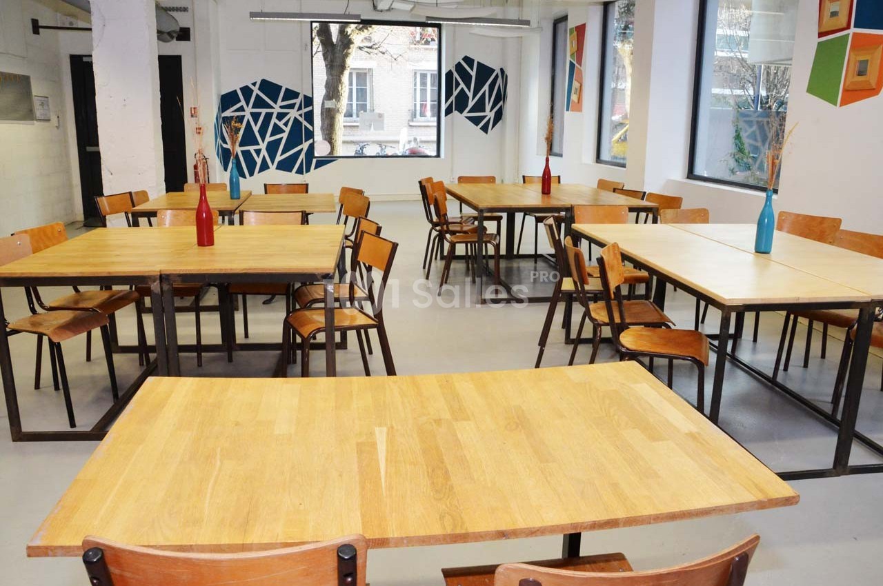 Salle lumineuse avec des tables en bois, des chaises en métal et des décorations murales géométriques colorées.