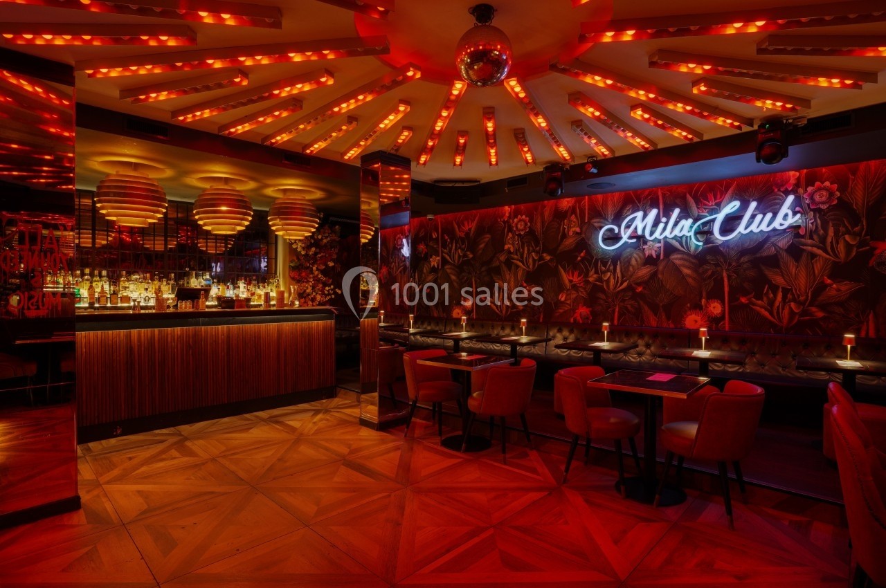 Intérieur d'un bar lounge avec éclairage tamisé, banquettes, tables, bar en bois et enseigne lumineuse au mur.