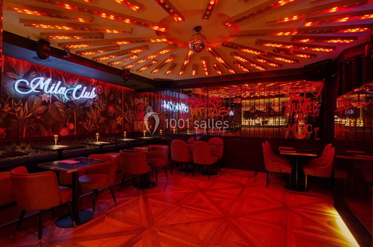 Salle de bar avec éclairage rouge, banquettes, tables et néons décoratifs sur les murs et le plafond.