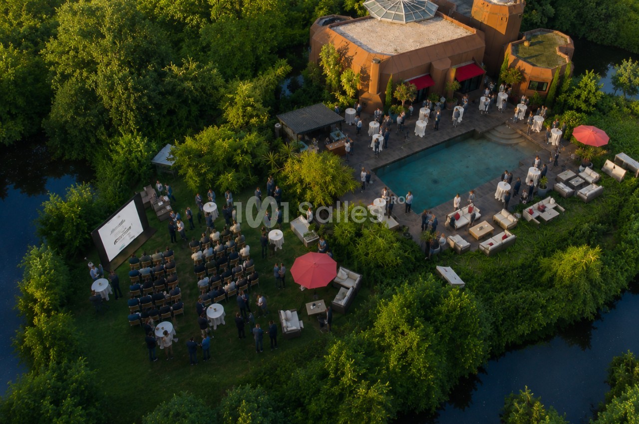 Vue aérienne d'un événement en plein air autour d'une piscine, avec des invités, des tables et une présentation sur écran.