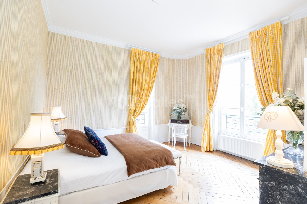 Chambre lumineuse avec lit double, parquet en bois, rideaux jaunes et bureau près d'une fenêtre.