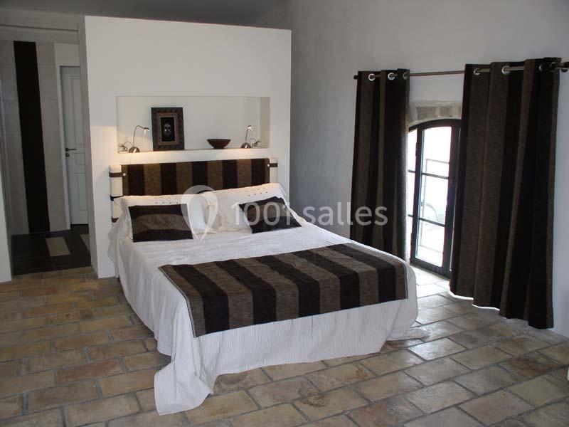 Chambre avec lit double, tête de lit rayée, sol en carrelage, rideaux sombres et fenêtre apportant de la lumière naturelle.